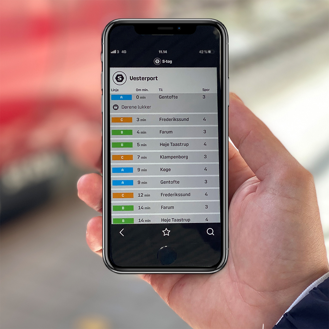 Hånd, der holder mobiltelefon med Banedanmarks app Din Station